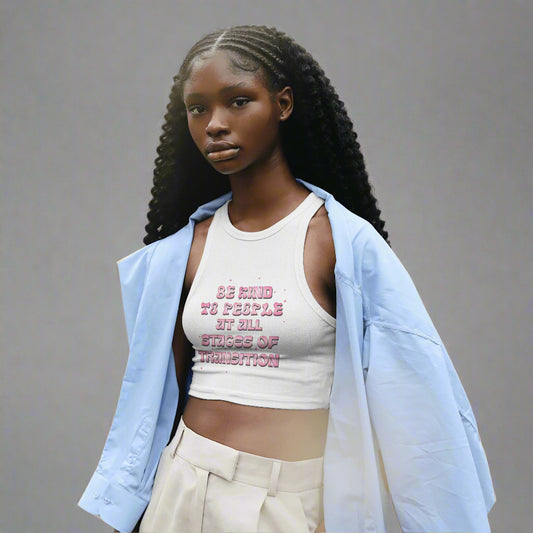 White fitted tank top with pink text reading “Be Kind to People at All Stages of Transition” in bold, bubbly letters